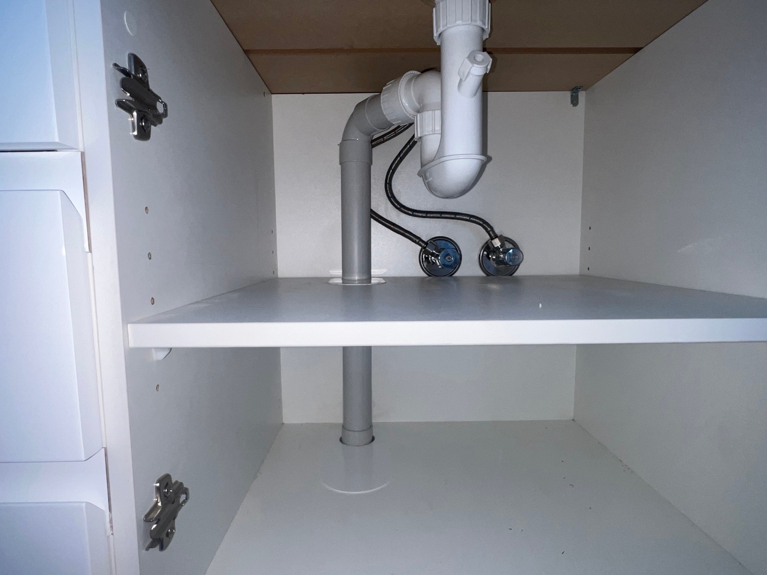 White basin trap, waste pipe and supply valves inside a cabinet.