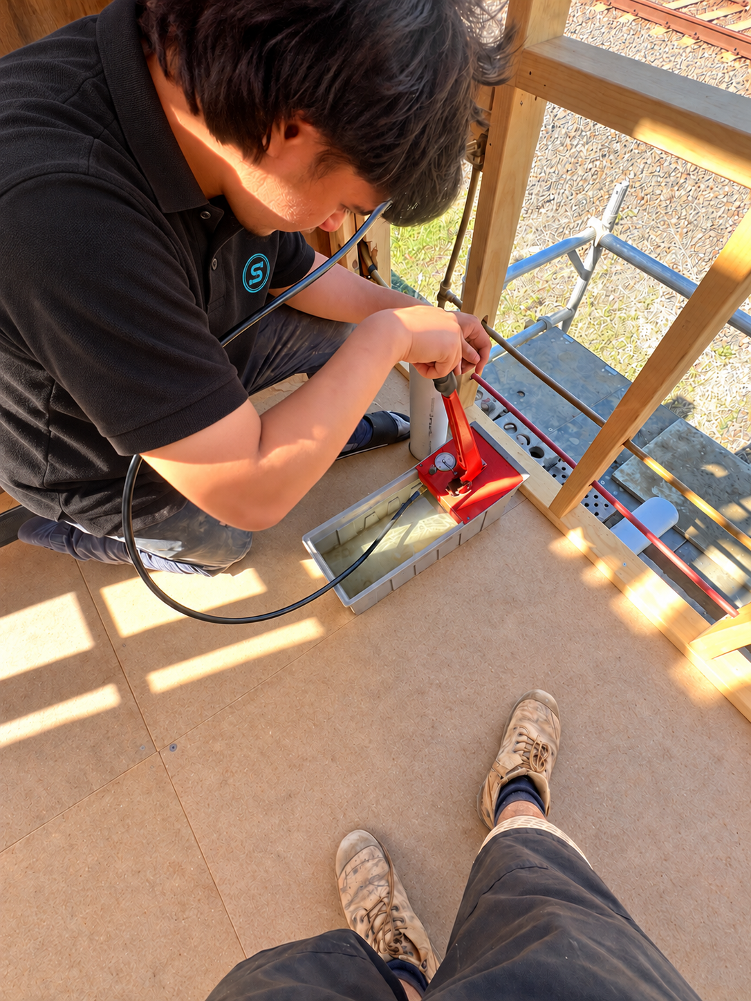 Pressure testing pipework with a hand pump in a timber-framed room.